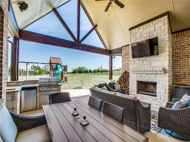 Covered outdoor living room with stone fireplace, dining table, and built-in grill